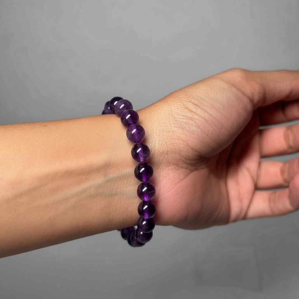 Hand wearing a purple beaded bracelet on a gray background