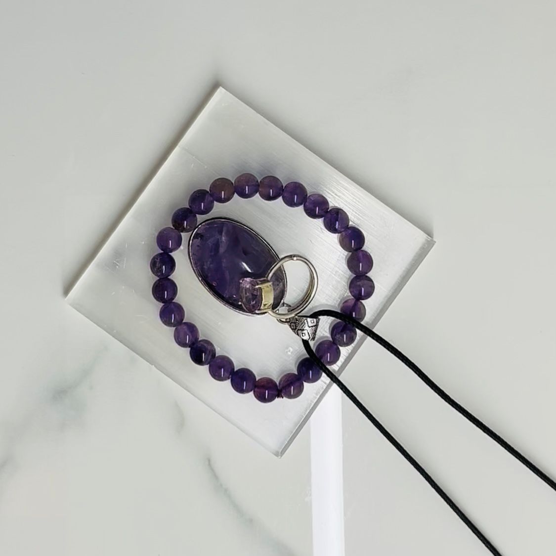 Purple beaded bracelet with a mirror and ring on a white surface