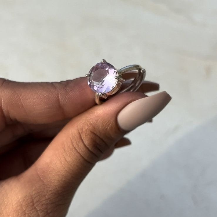 Hand holding a ring with amethyst gemstone against a neutral background