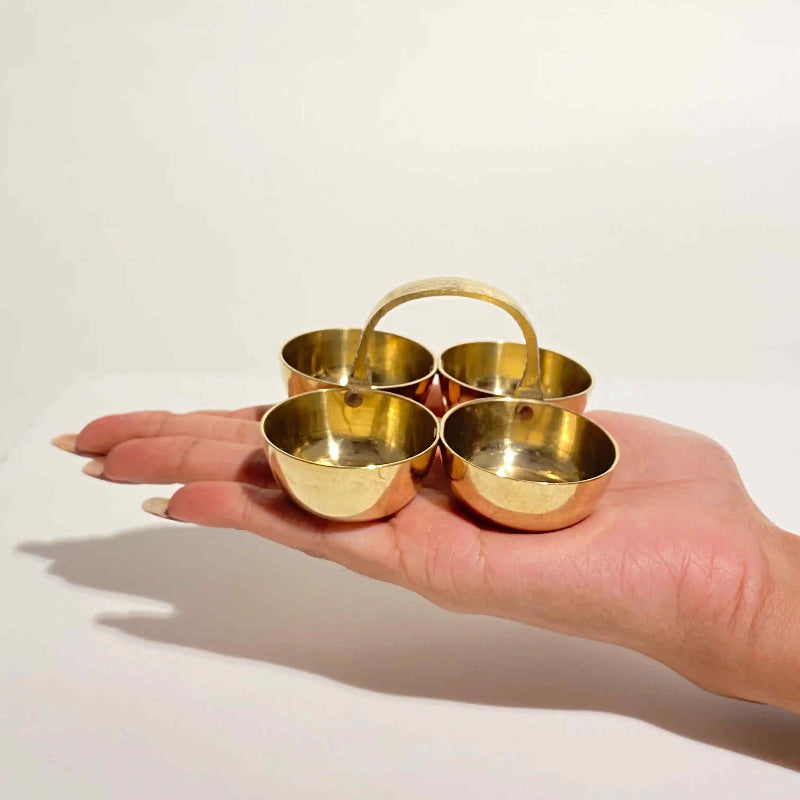 Hand holding a set of four small brass bowls on a light background