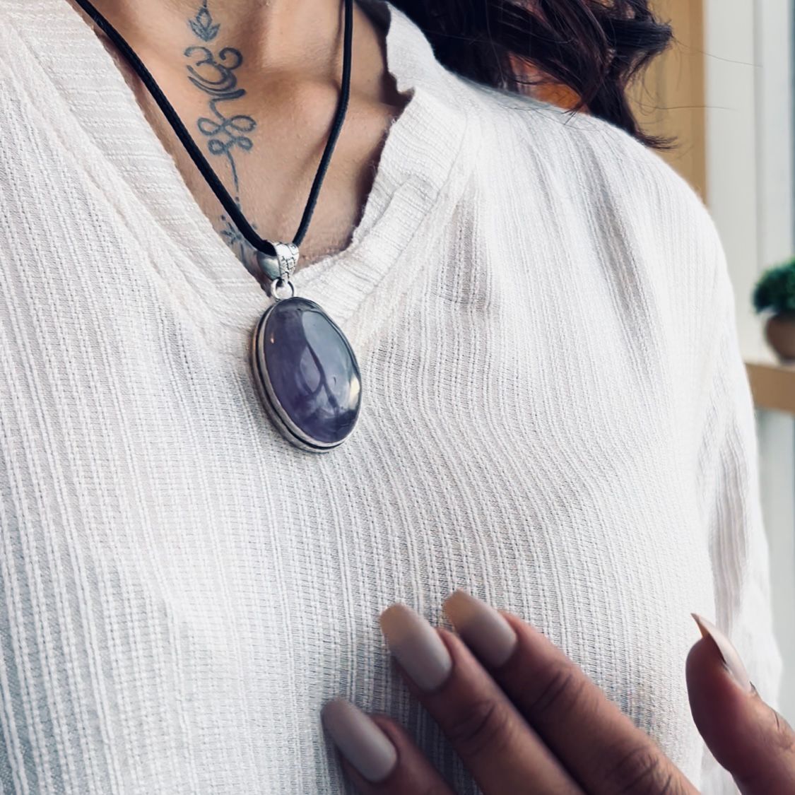 Person wearing a necklace with a purple pendant on a white shirt.