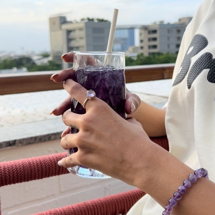 Person holding a purple drink with a straw on a balcony with cityscape in the background