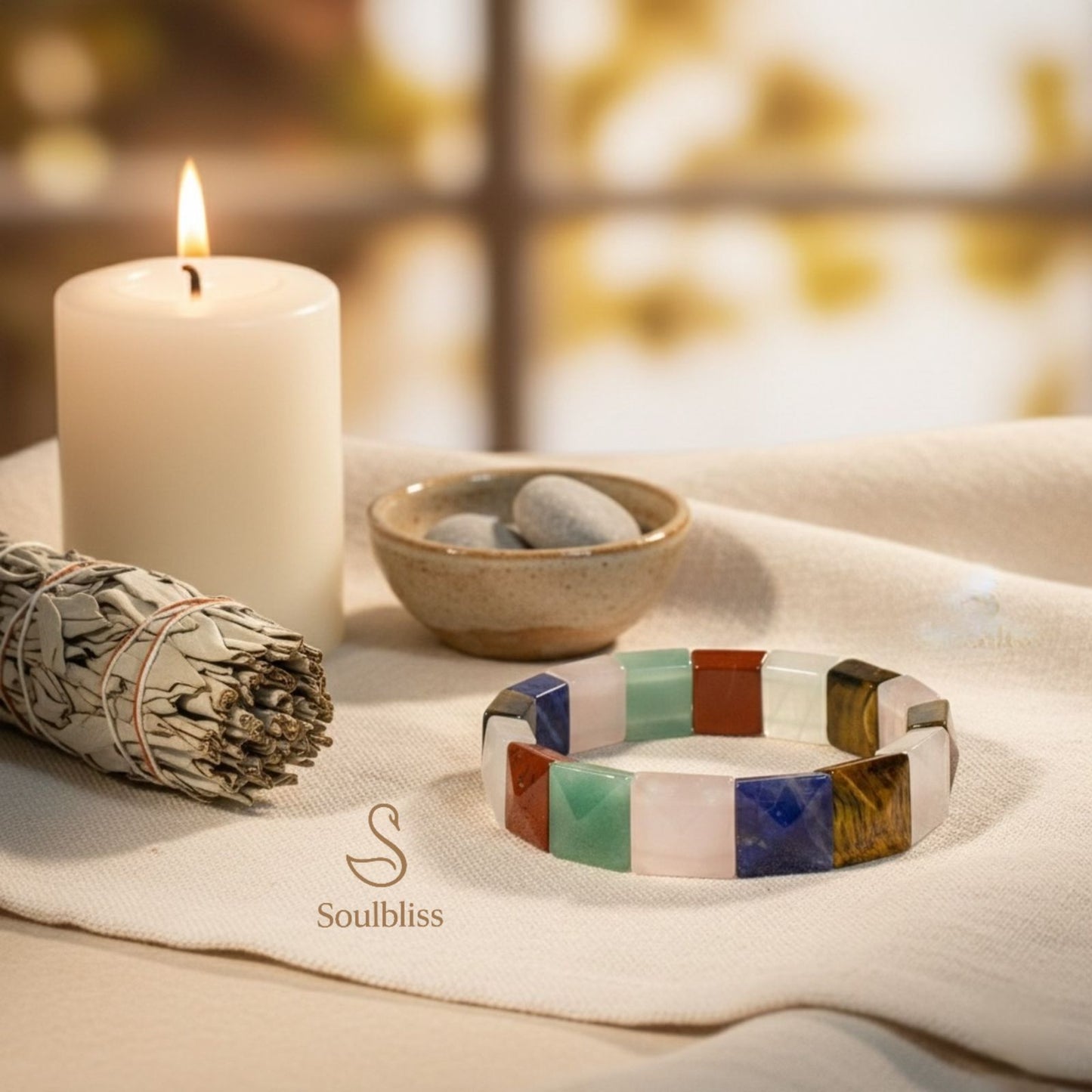Colorful gemstone bracelet on a cloth with a candle, smudge stick, and stones in the background.