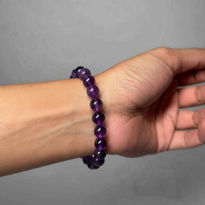 Hand wearing a purple beaded bracelet on a gray background