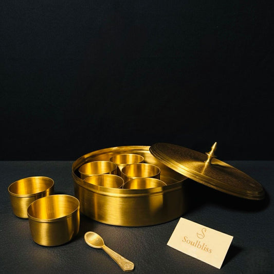Gold metal container with compartments and a spoon on a dark surface, featuring the brand 'Staubbliss'.