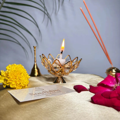 Decorative setup with a lit candle in a gold holder, flowers, and incense sticks on a textured surface.
