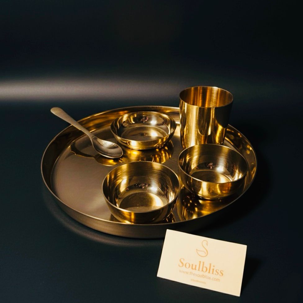 Gold dining set with bowls, cups, and a spoon on a dark background, featuring the brand 'Soulbliss'.
