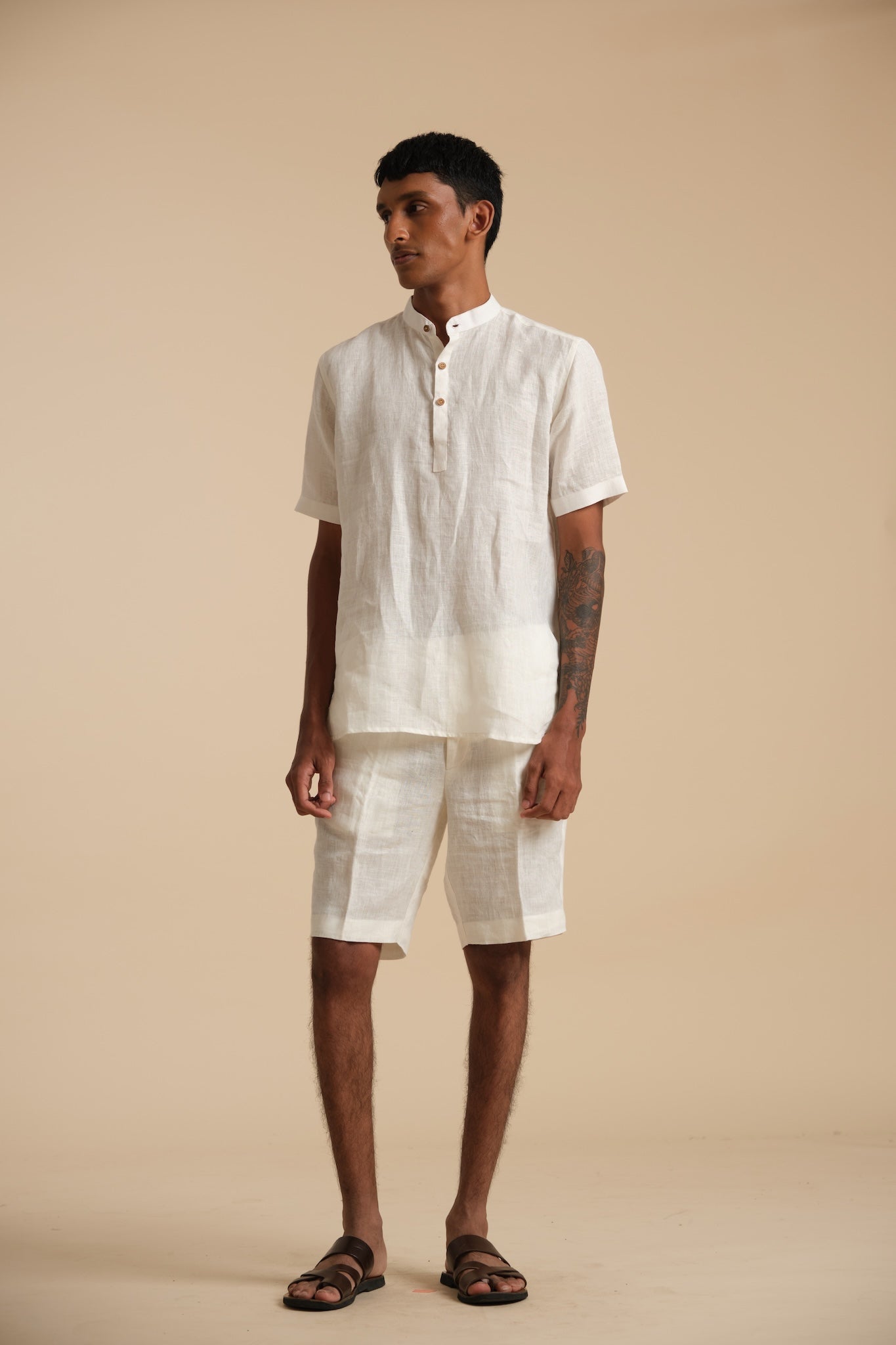 Man wearing a white linen shirt and shorts on a beige background