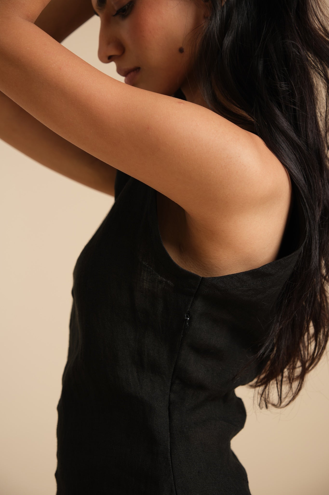Woman wearing a black sleeveless linen top against a beige background