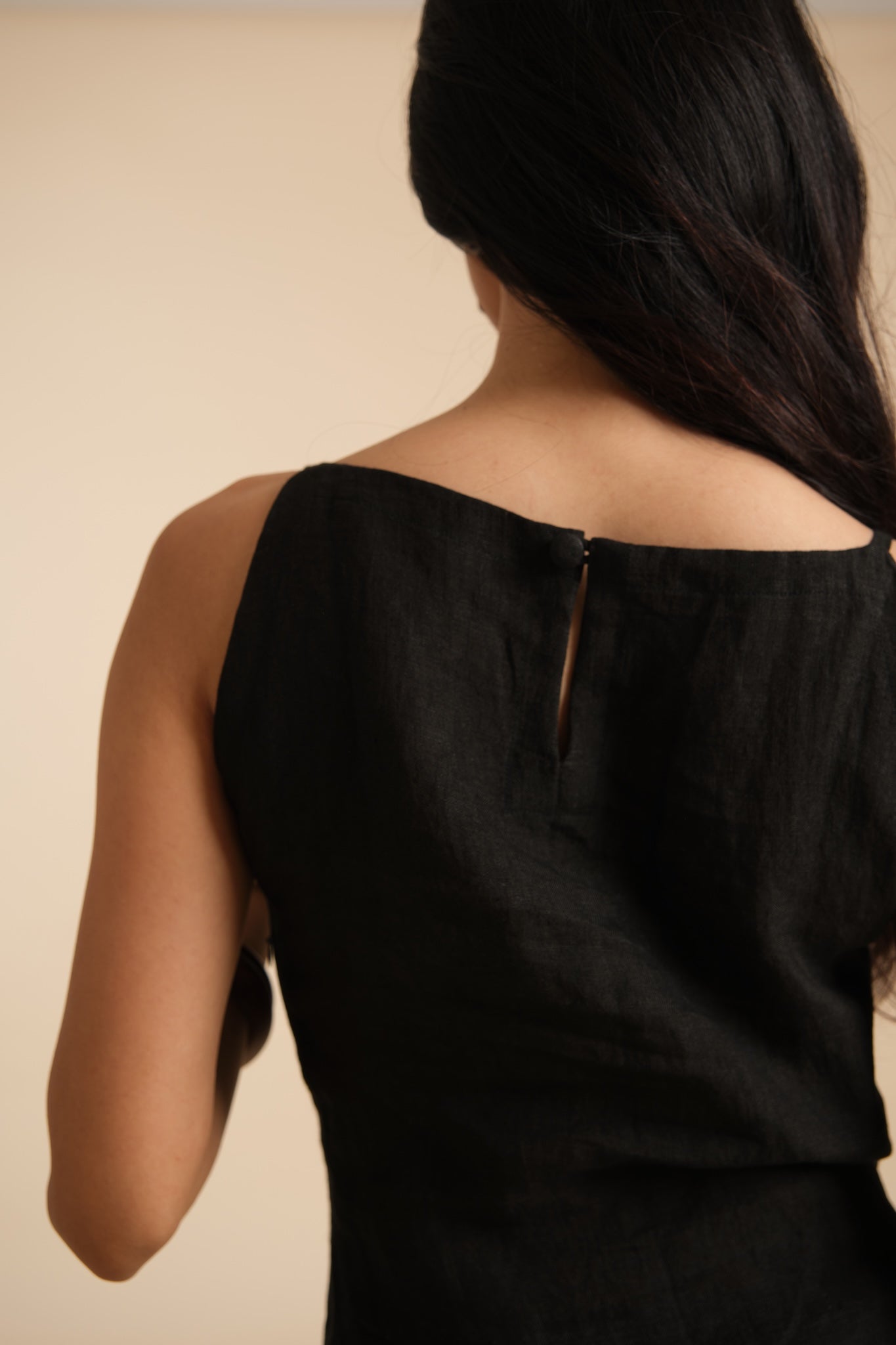 Black linen sleeveless top worn by a person on a beige background