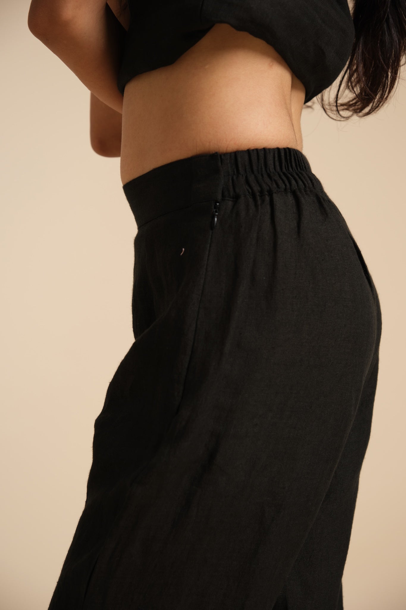 Person wearing black high-waisted linen pants on a beige background