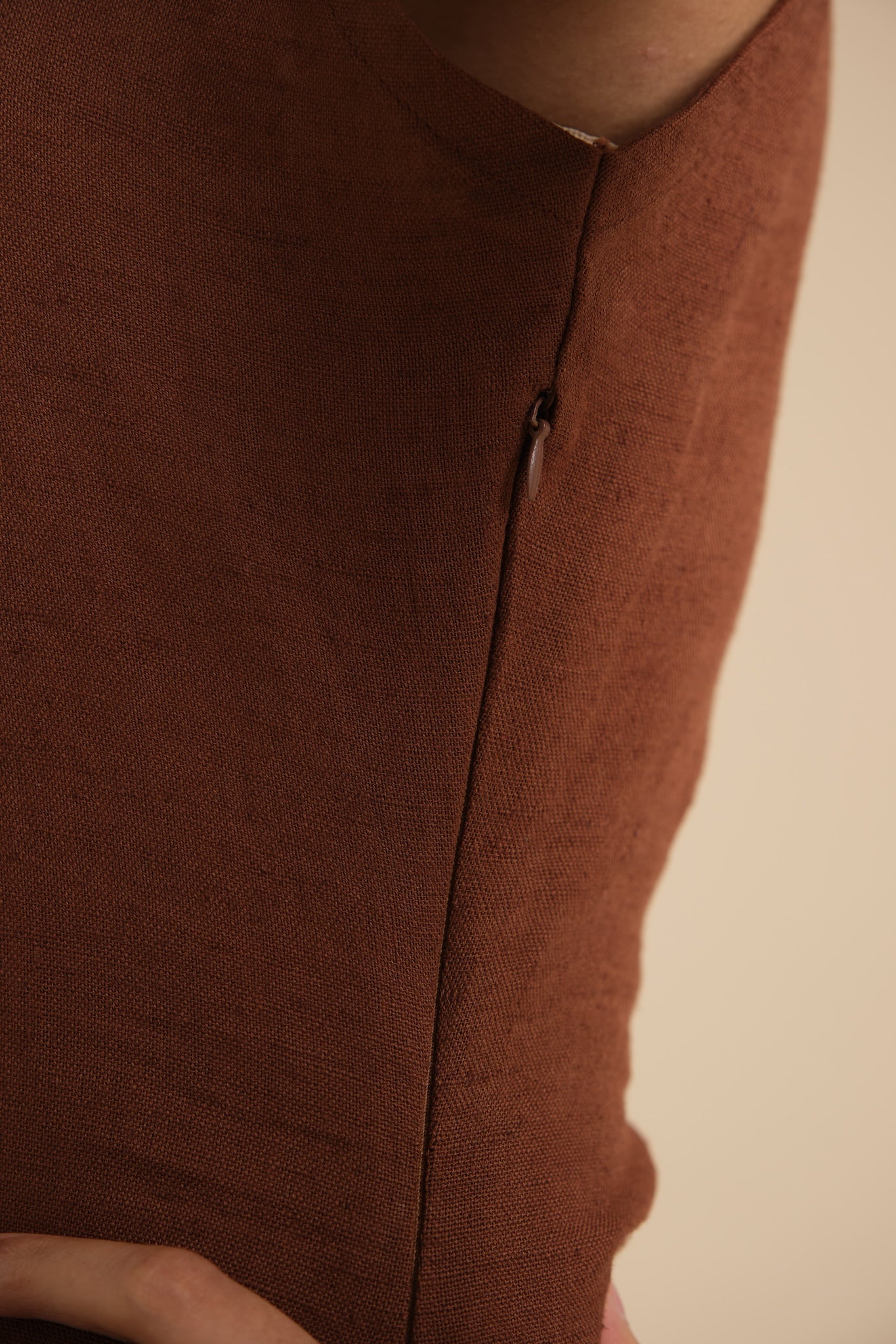 Close-up of a brown linen garment with a zipper on a beige background