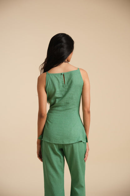 Woman wearing a green sleeveless top and pants against a beige background