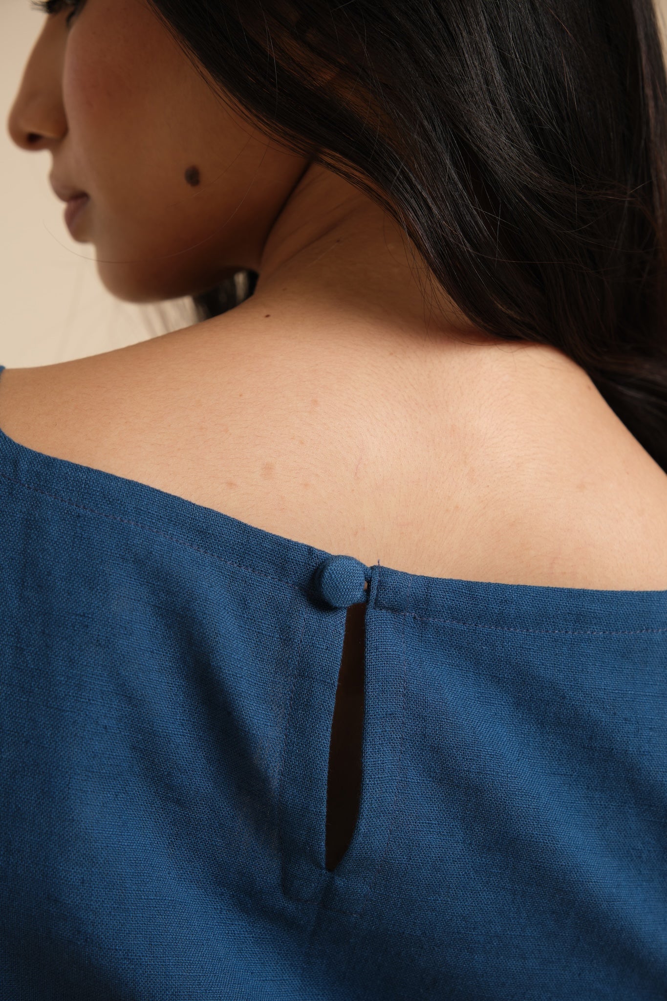 Close-up of a person wearing a blue off-shoulder top with a neutral background