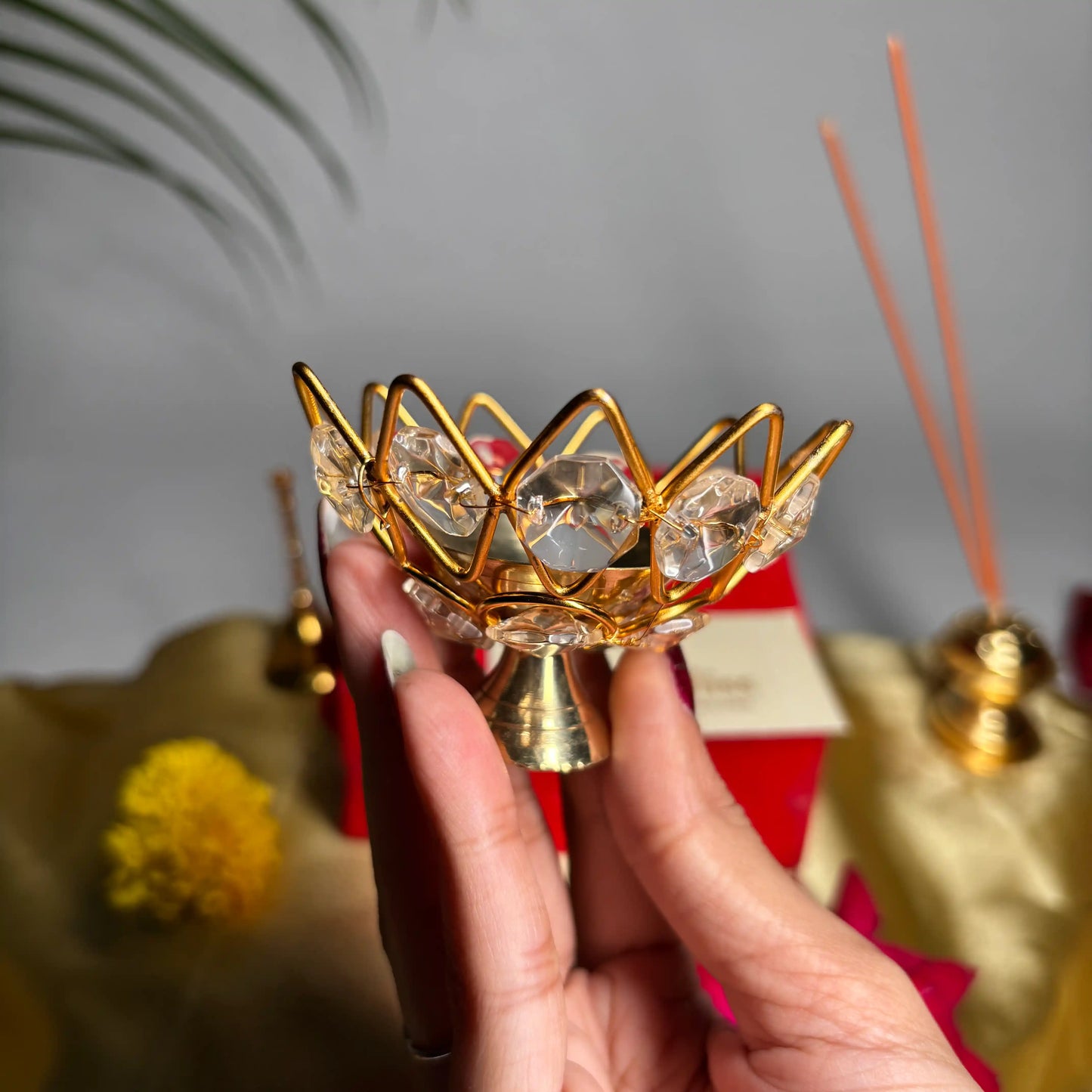 Hand holding a decorative gold and crystal incense holder with a blurred background