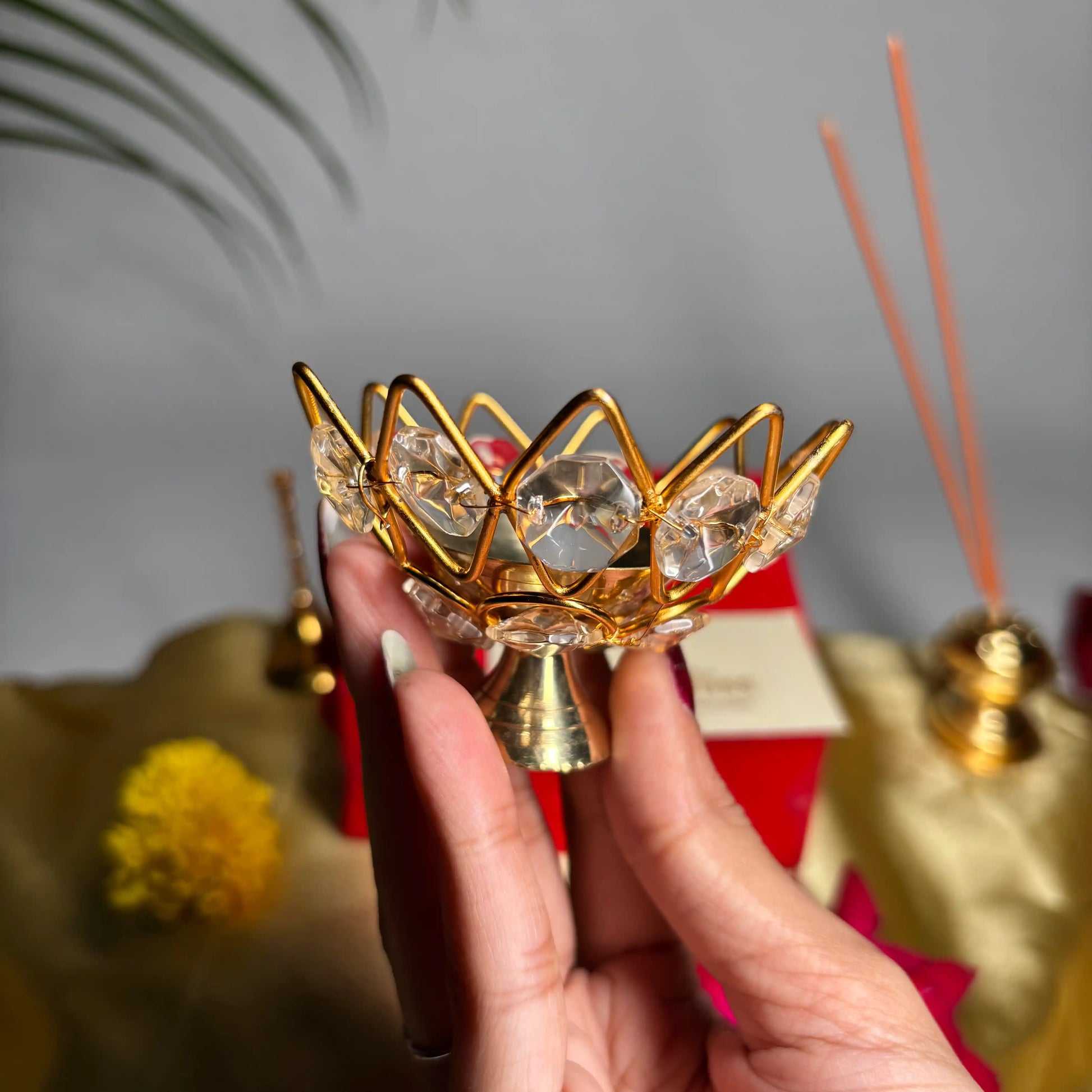 Hand holding a decorative gold and crystal incense holder with a blurred background