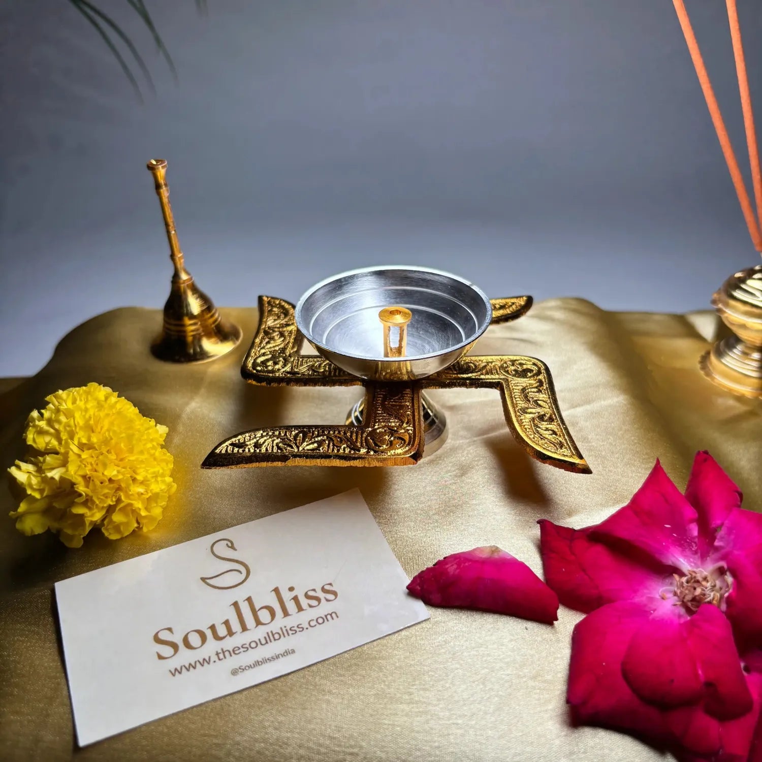 Decorative setting with a candle holder, flowers, and a 'Soulbliss' card on a textured surface.
