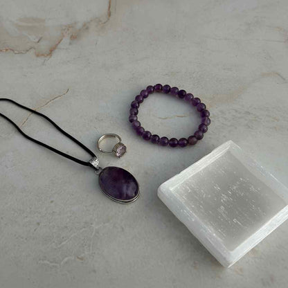 Amethyst jewelry set with necklace, bracelet, and ring on a marble surface