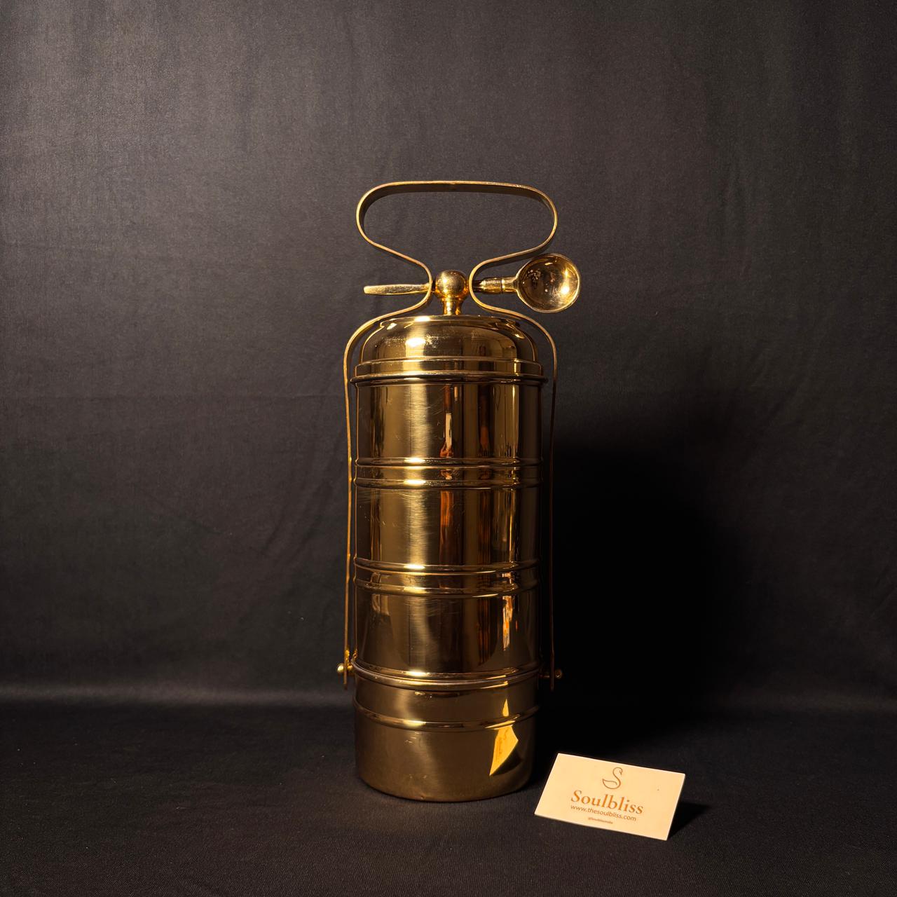 Brass tiffiin on a dark background with a visible brand label.