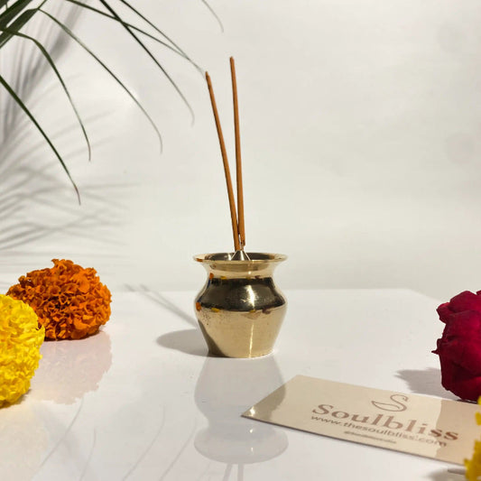 Gold vase with incense sticks on a white surface with flowers and a 'Soulbliss' card.