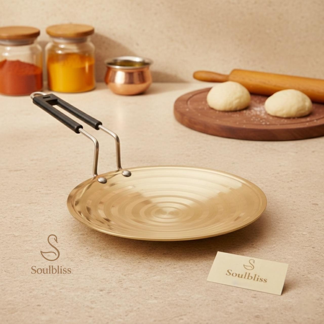 Gold frying pan with black handle on a beige surface, surrounded by kitchen items and a 'Soulbliss' card.