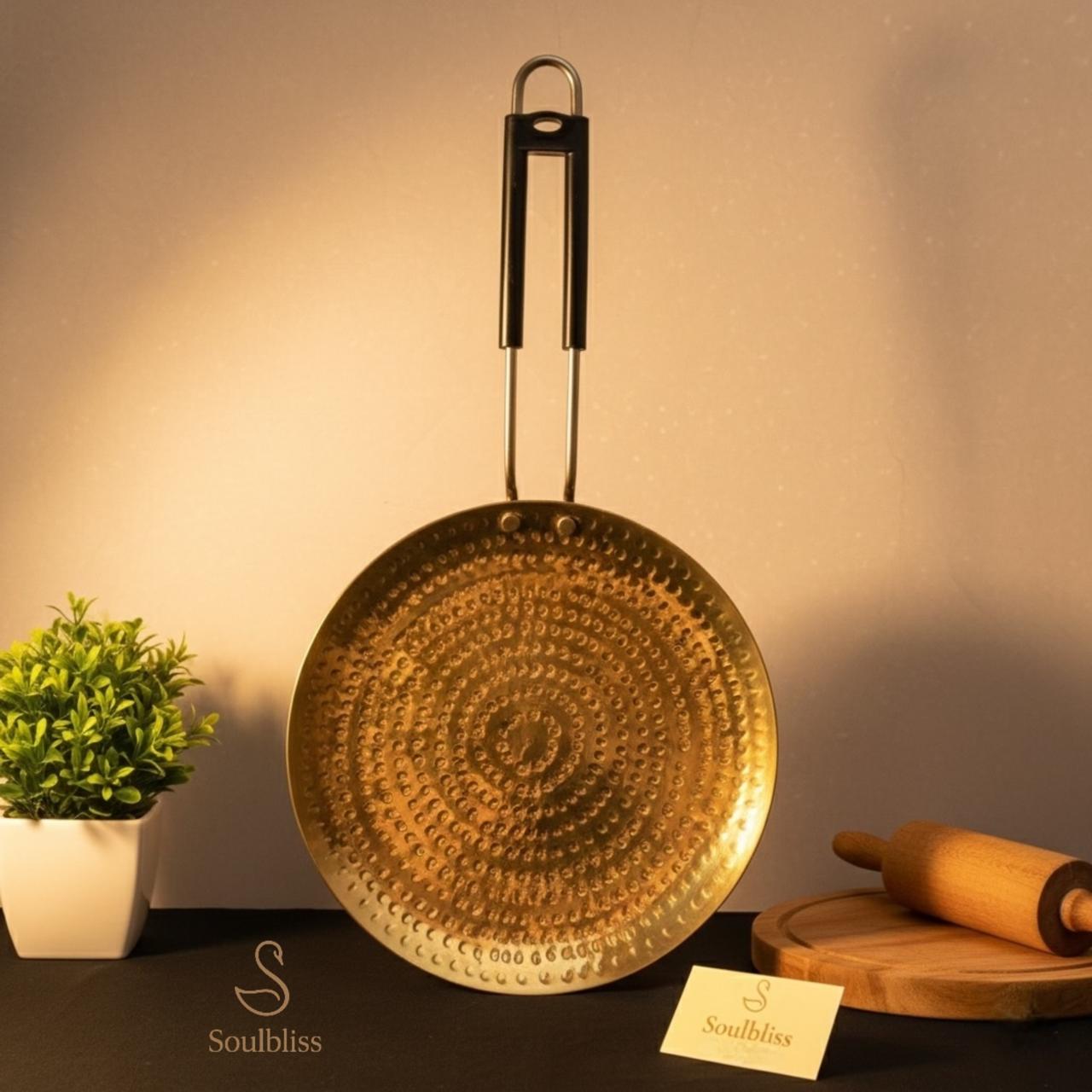 Decorative gold pan with a plant and rolling pin on a dark surface, branded 'Soulbliss'.