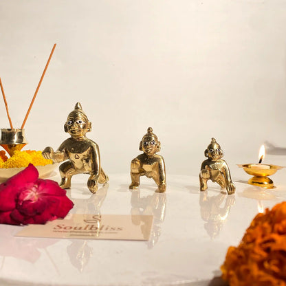 Gold figurines on a white surface with incense sticks, flowers, and a candle.