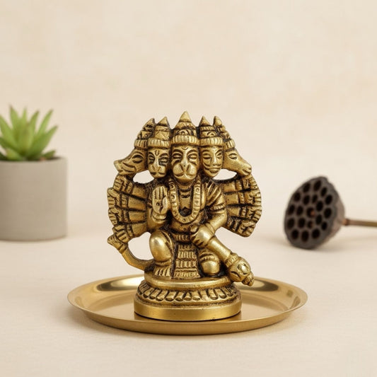 brass statue of panchmukhi hanumanji on a small platform with a plant and object in the background