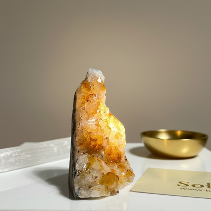Citrine crystal on a white surface with a gold bowl and card in the background