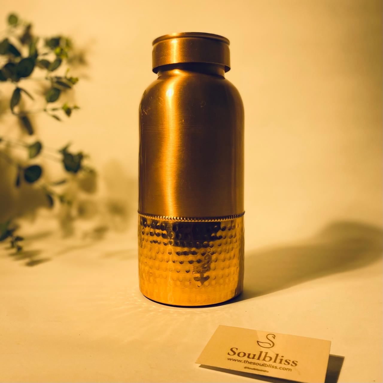 Gold-colored water bottle with 'Soulbliss' branding on a light surface with a blurred plant in the background.