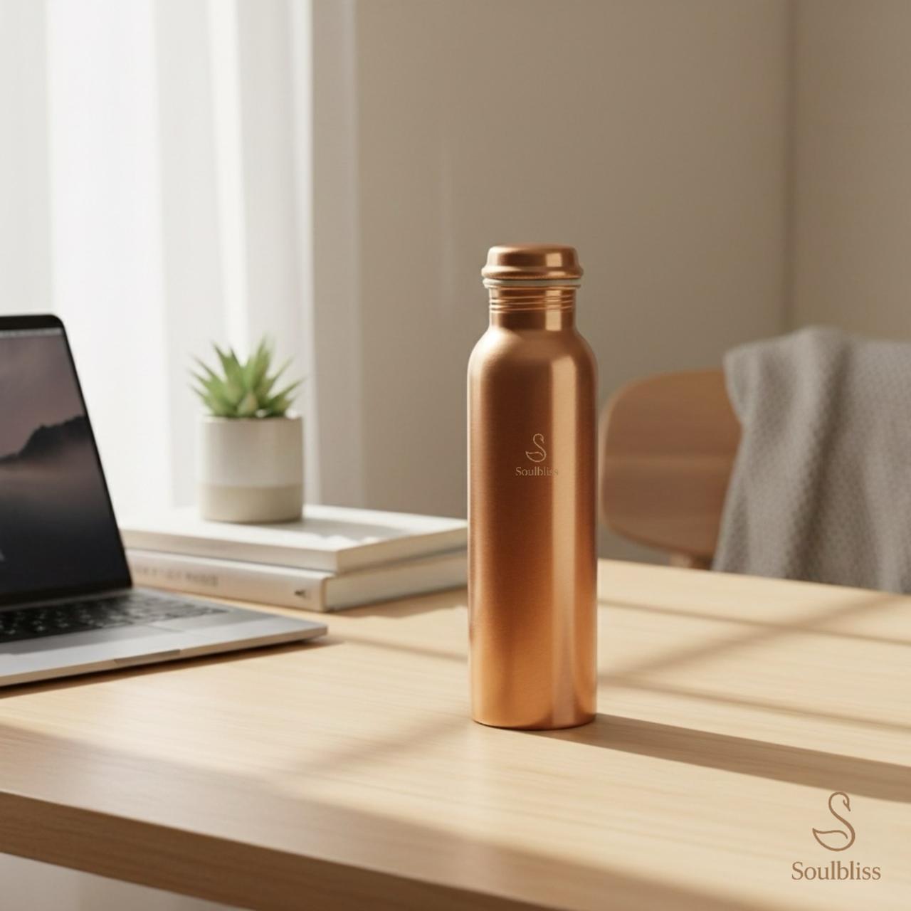 copper water bottle on a wooden desk with a laptop and plant in the background