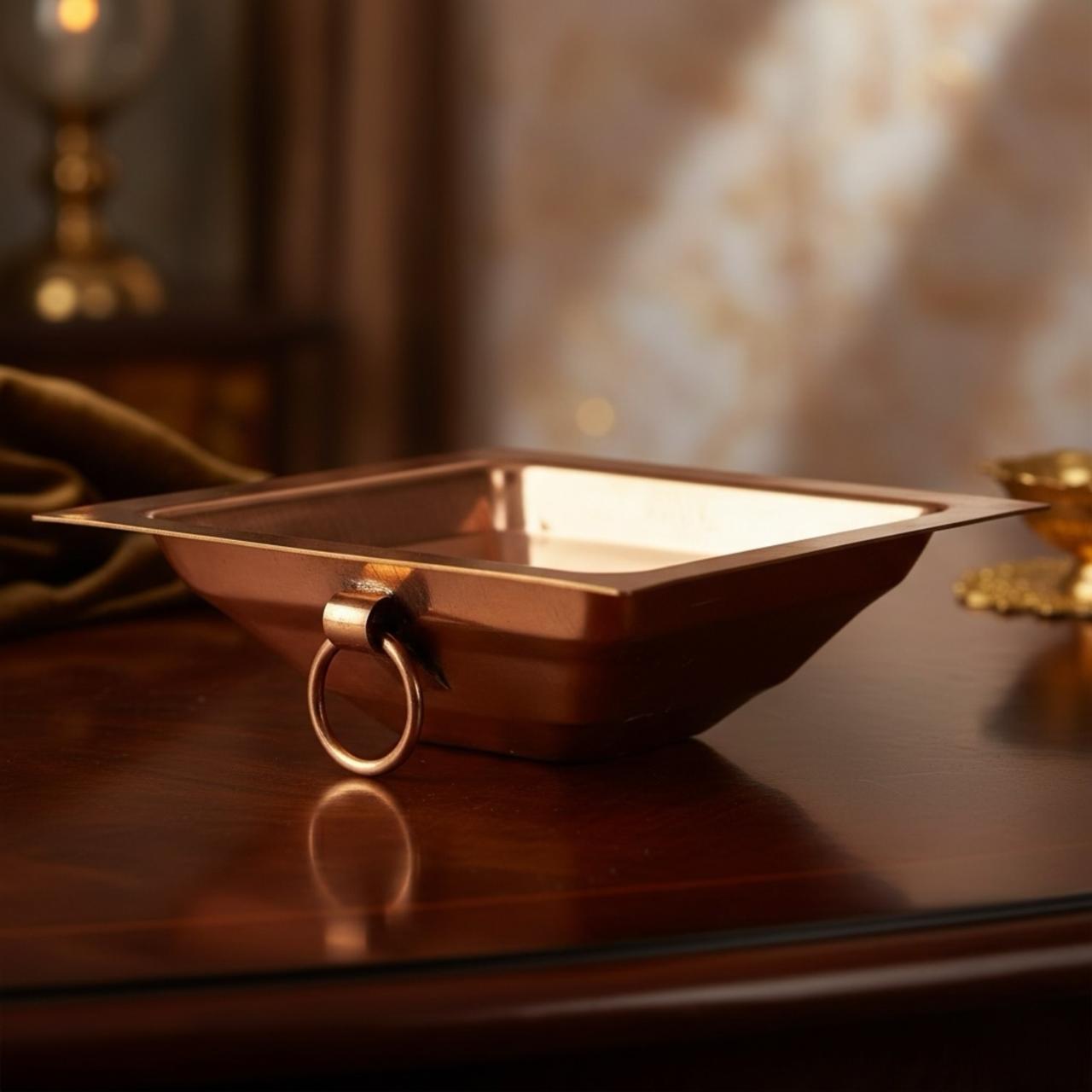 Copper thavan kund with ring handle on a reflective surface