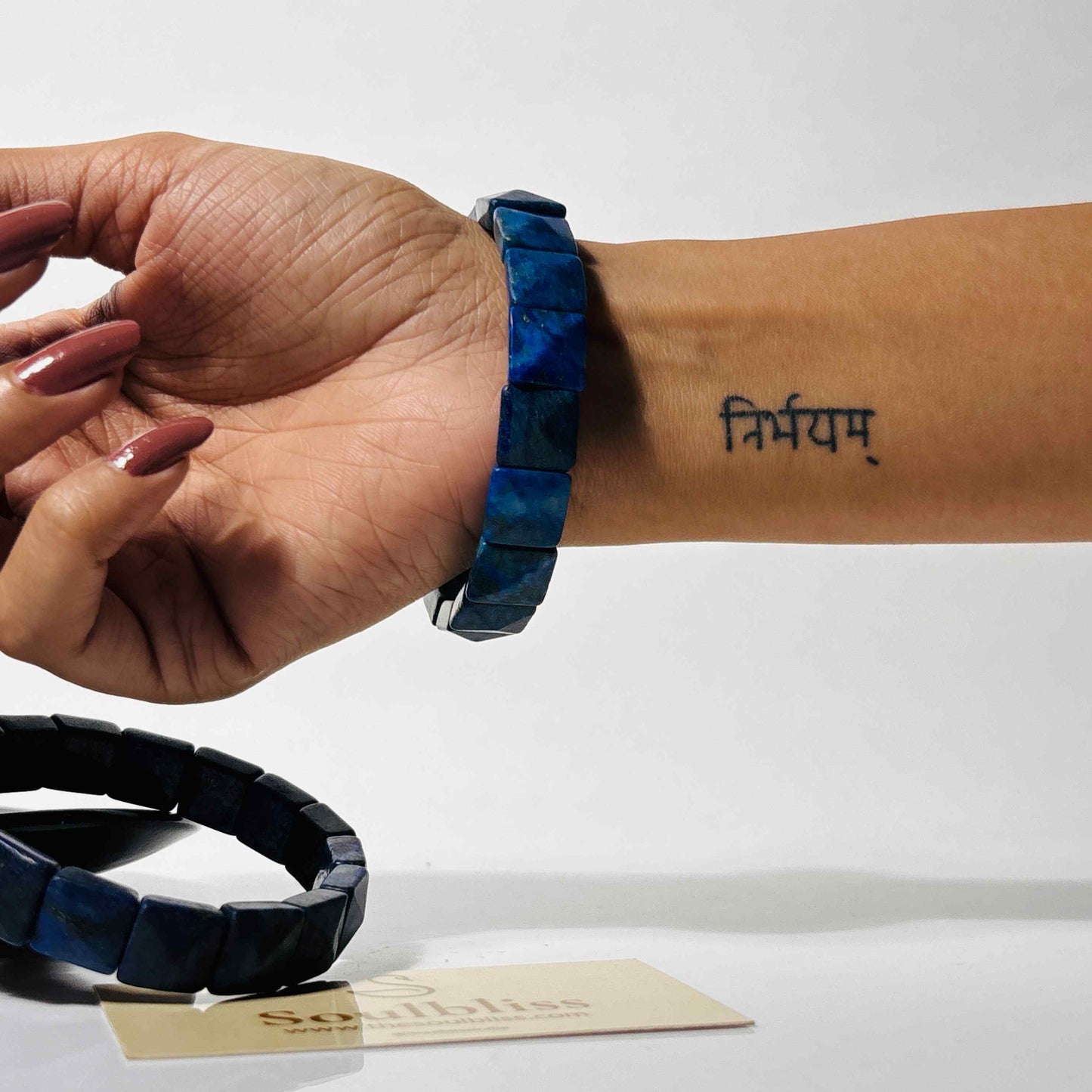 Person wearing a blue bracelet with a visible tattoo on wrist, against a white background