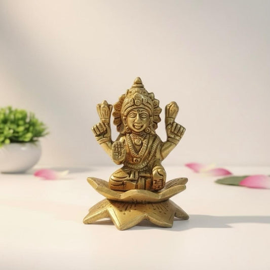 Gold-colored laxmi statue of a seated figure on a white background with a plant and petals.
