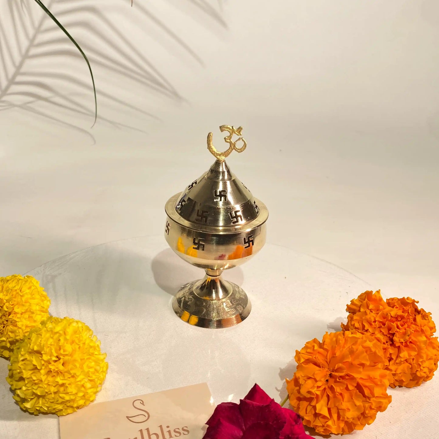 Silver incense burner with yellow and orange marigold flowers on a white surface