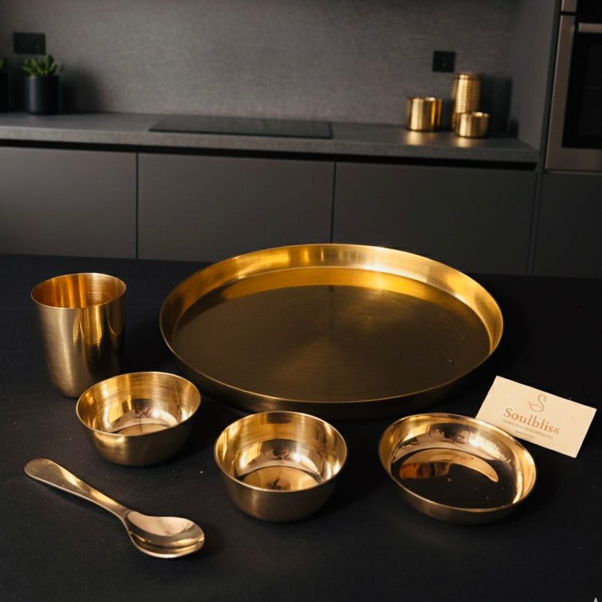 Set of gold kitchenware including a tray, bowls, and a spoon on a dark surface.
