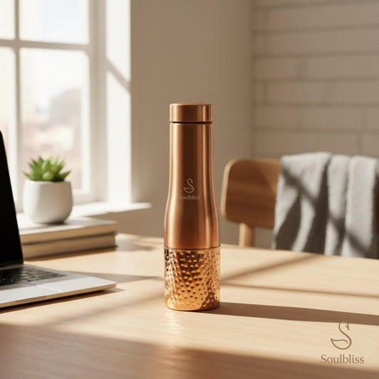 Rose gold water bottle on a desk with a laptop and plant in the background